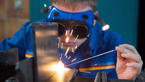 Una persona sta saldando su un banco da lavoro.  © dpa-Bildfunk Foto: Sebastian Kanert