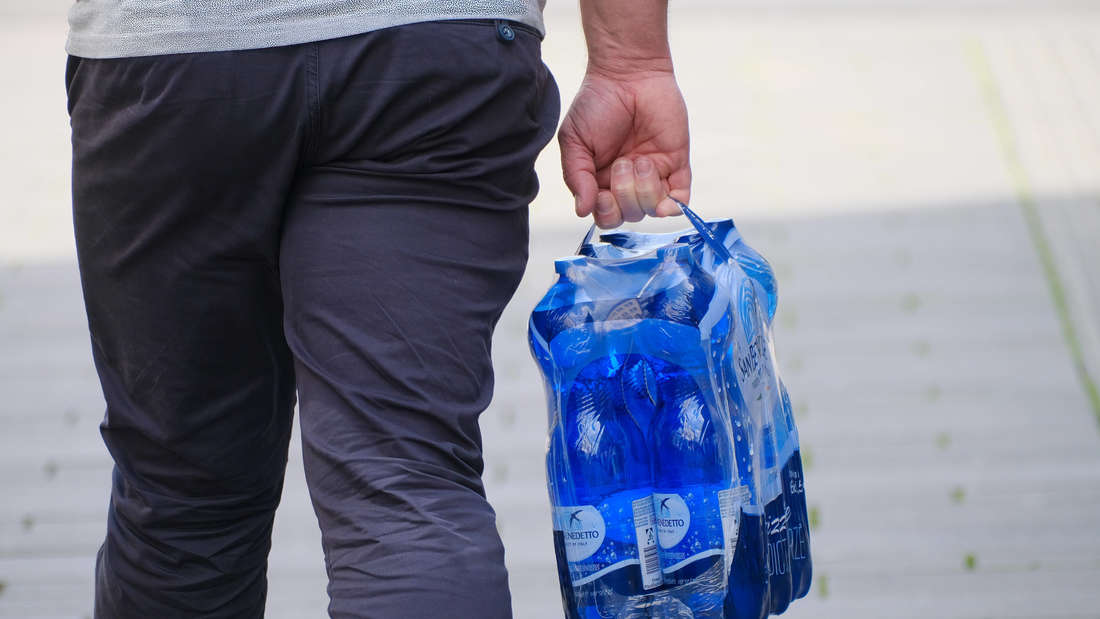 Dopo la spesa al supermercato: un uomo tiene in mano sei lattine di acqua minerale.