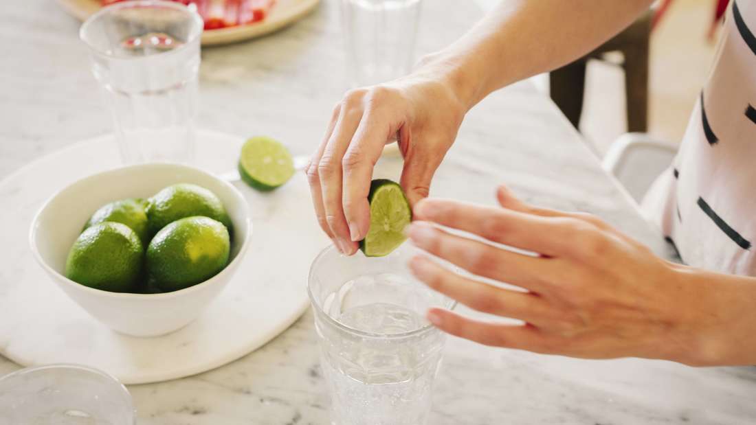 Una persona mette un limone in un bicchiere d'acqua.