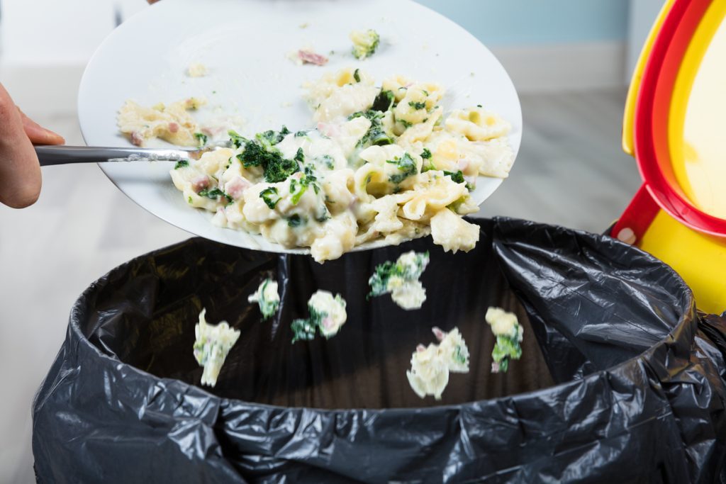 Eine Person wirft Speisereste von einem Teller in den Mülleimer