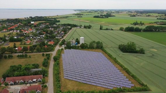 Vista dall'alto: un grande impianto fotovoltaico multi-array in piedi in un campo in una zona costiera rurale.  © Schermata 
