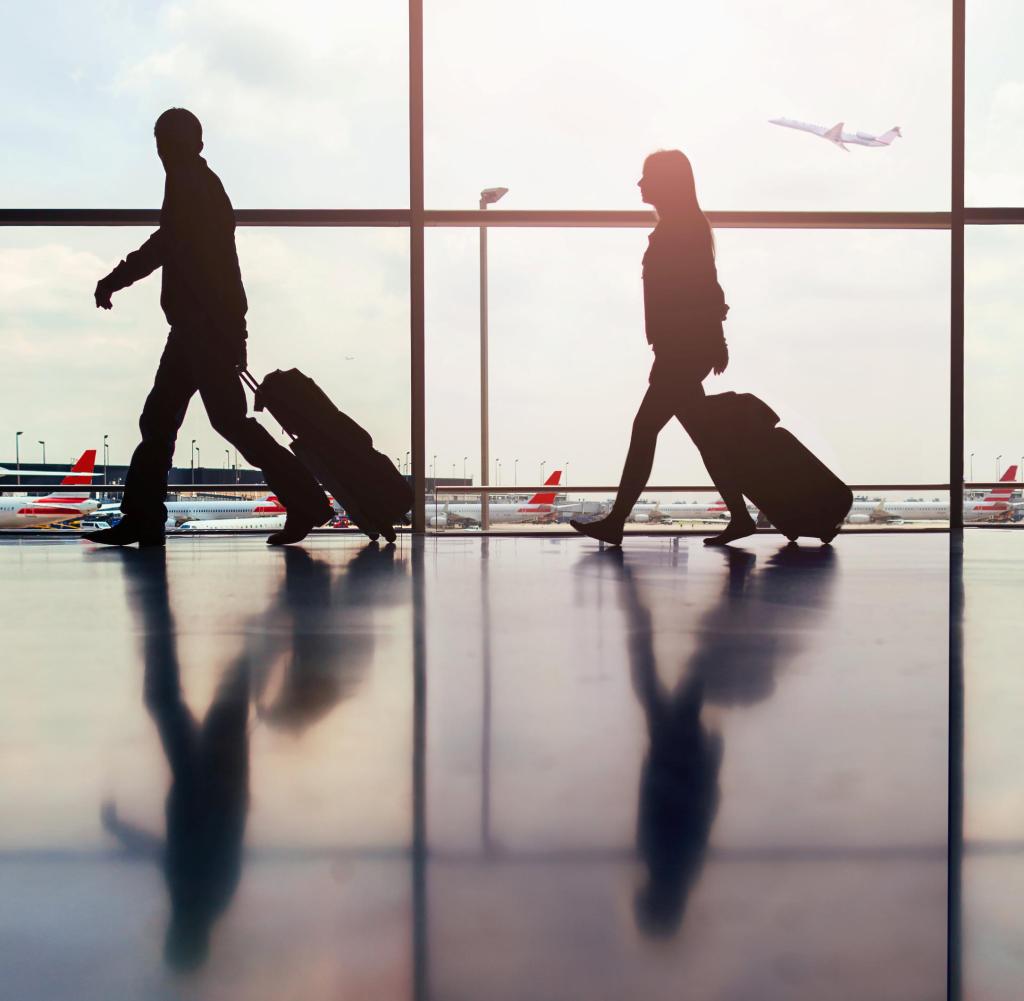 Silhouette di due passeggeri che camminano attraverso l'ingresso dell'aeroporto con i bagagli.  Getty ImagesGetty Images
