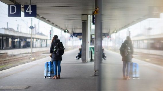 Una donna aspetta con una valigia sul binario 4 della stazione centrale di Hannover con l'immagine riflessa in una lastra di vetro.  © dpa bildfunk Foto: Julian Stratensholt